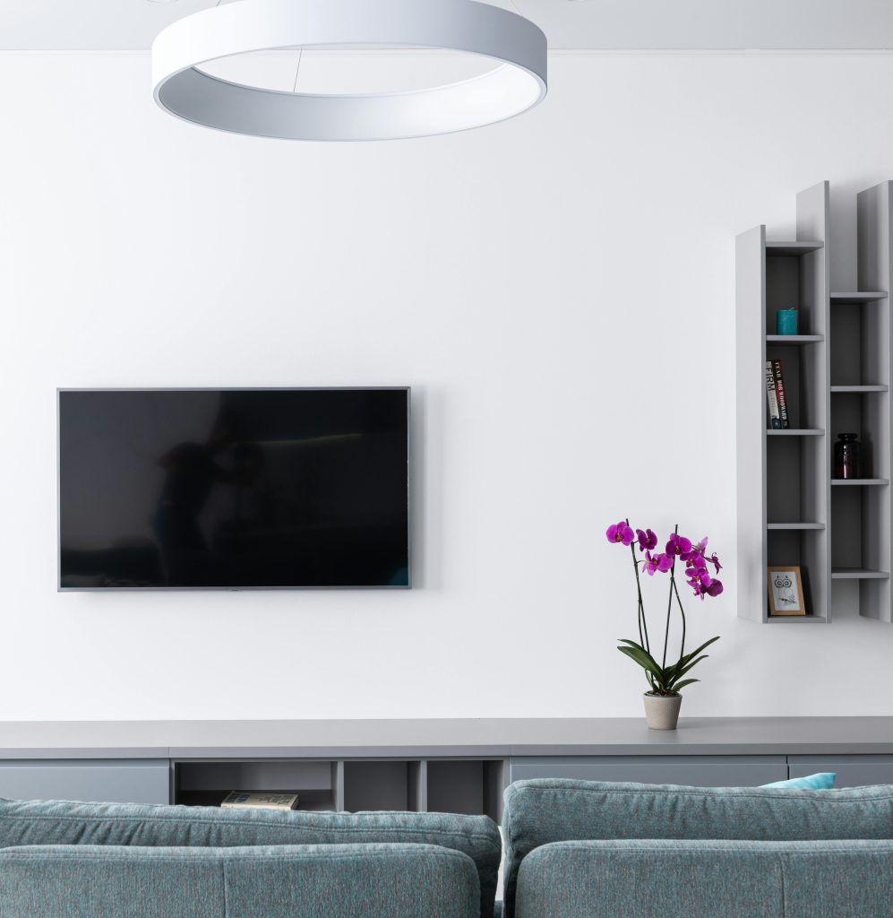 Comfortable modern living room with gray sofa and TV with shelves hanging on wall